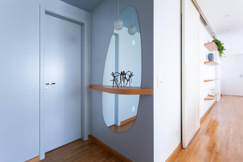 Base neutra com pontos marcantes em azul definem apê de 167 m². Projeto de Ju Miranda. Na foto, hall de entrada azul, espelho em formato orgânico, prateleira flutuante.