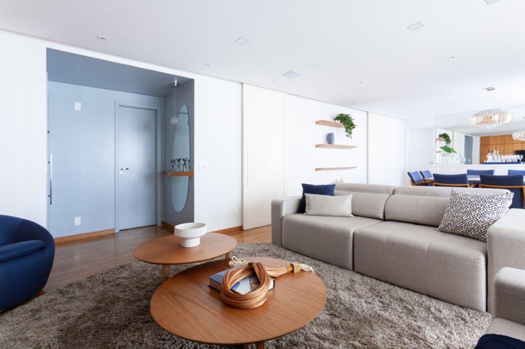 Base neutra com pontos marcantes em azul definem apê de 167 m². Projeto de Ju Miranda. Na foto, sala de estar, sofá, mesa de centro de madeira, hall de entrada azul.