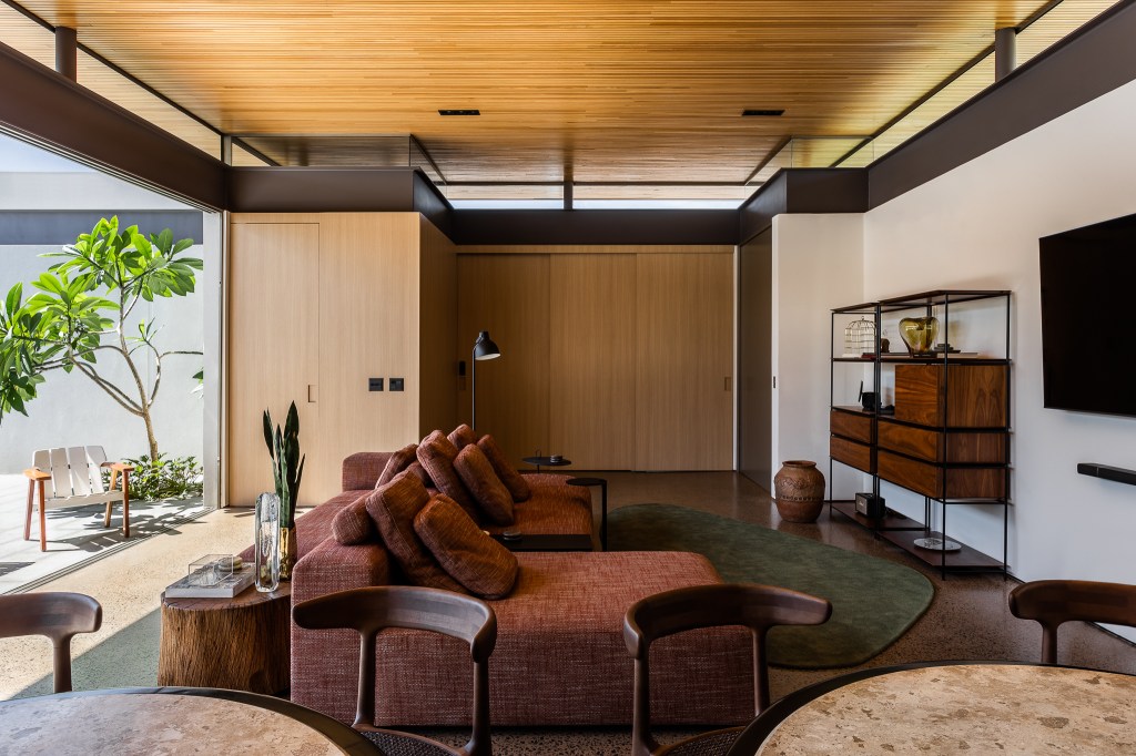 Casa de 168 m² em terreno triangular possui duas partes com usos distintos. Projeto de Studio Porto. Na foto, living com painéis de madeira e estante.