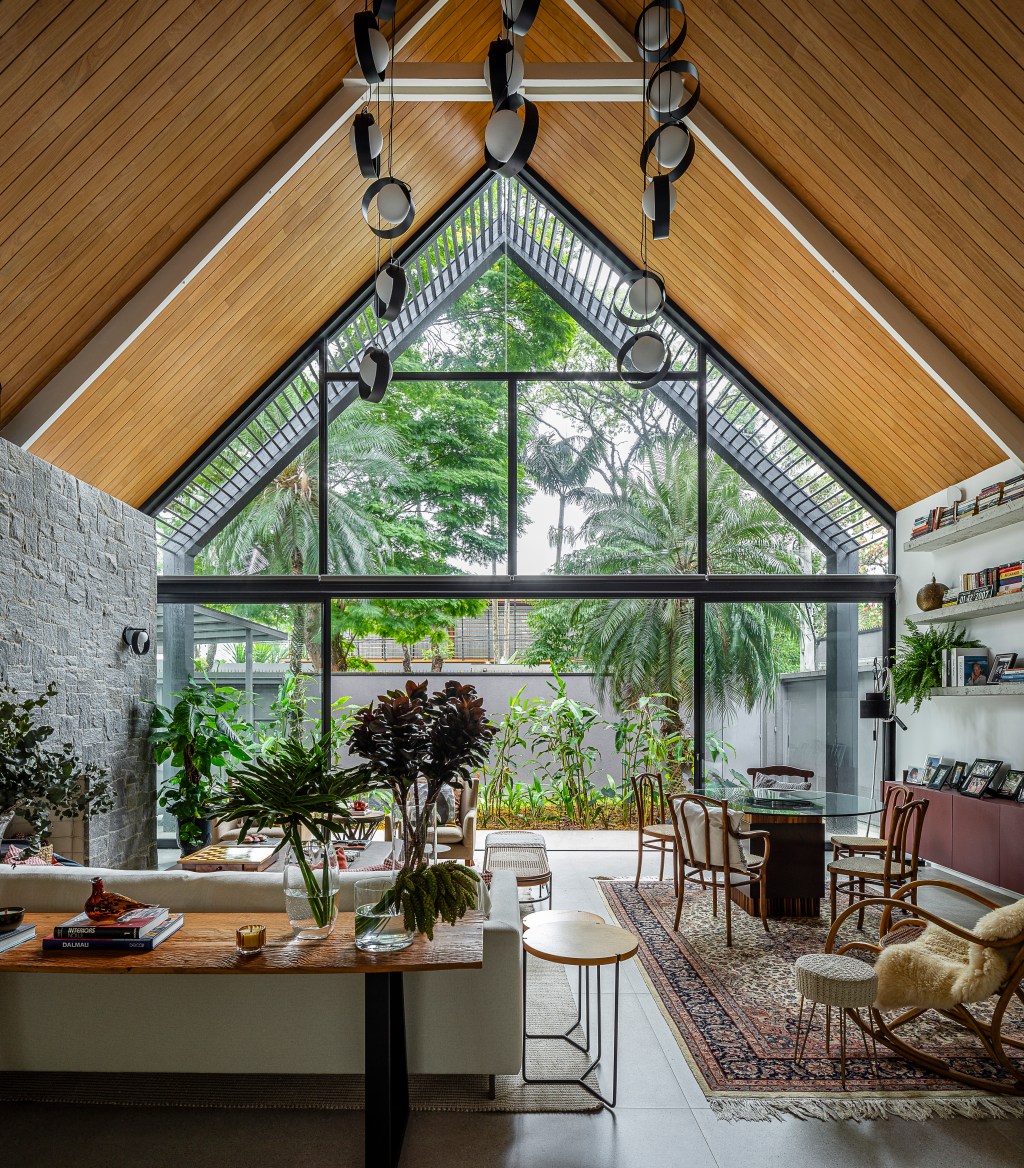 Casa de 415 m² com mezanino e varanda gourmet é inspirada em chalé alemão. Projeto de Arkitito Arquitetura. Na foto, sala com grandes janelas, teto com duas águas.