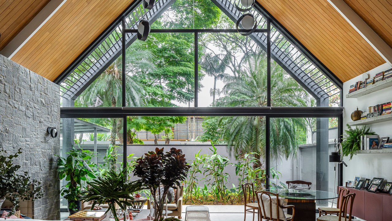 Casa de 415 m² com mezanino e varanda gourmet é inspirada em chalé alemão. Projeto de Arkitito Arquitetura. Na foto, sala com grandes janelas, teto com duas águas.