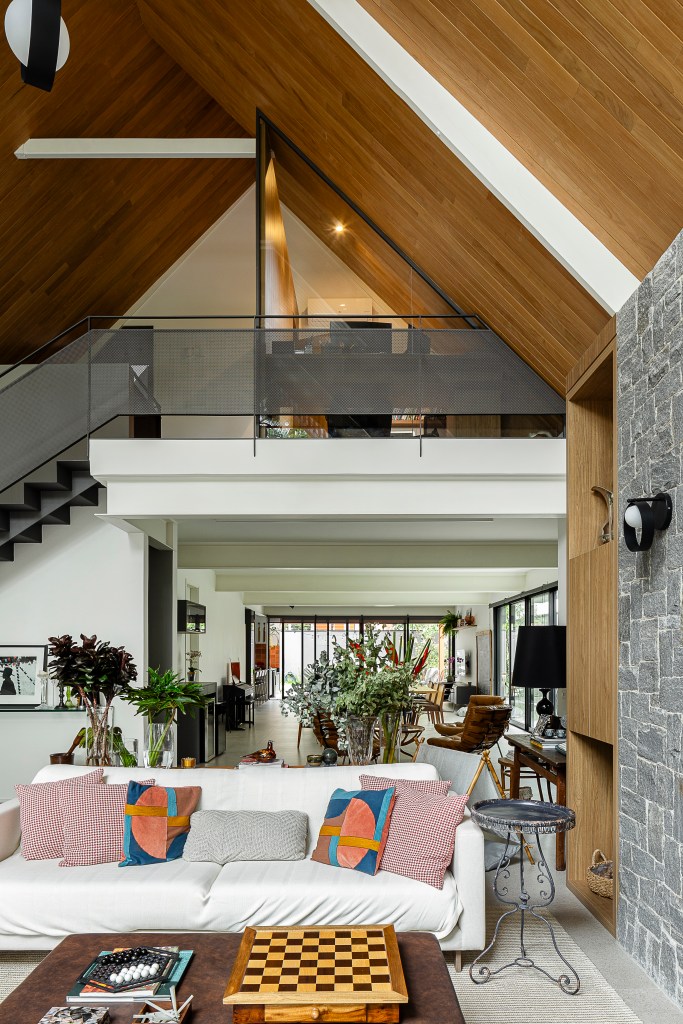 Casa de 415 m² com mezanino e varanda gourmet é inspirada em chalé alemão. Projeto de Arkitito Arquitetura. Na foto, sala com pé-direito alto, mezanino, sofá branco.