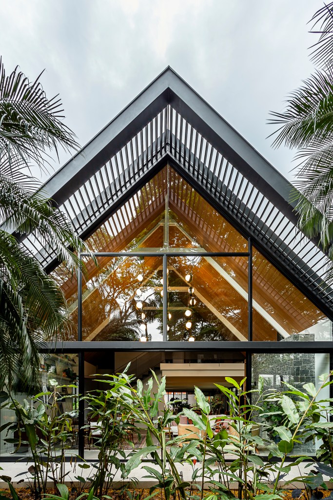 Casa de 415 m² com mezanino e varanda gourmet é inspirada em chalé alemão. Projeto de Arkitito Arquitetura. Na foto, fachada de casa, parede de vidro, plantas.