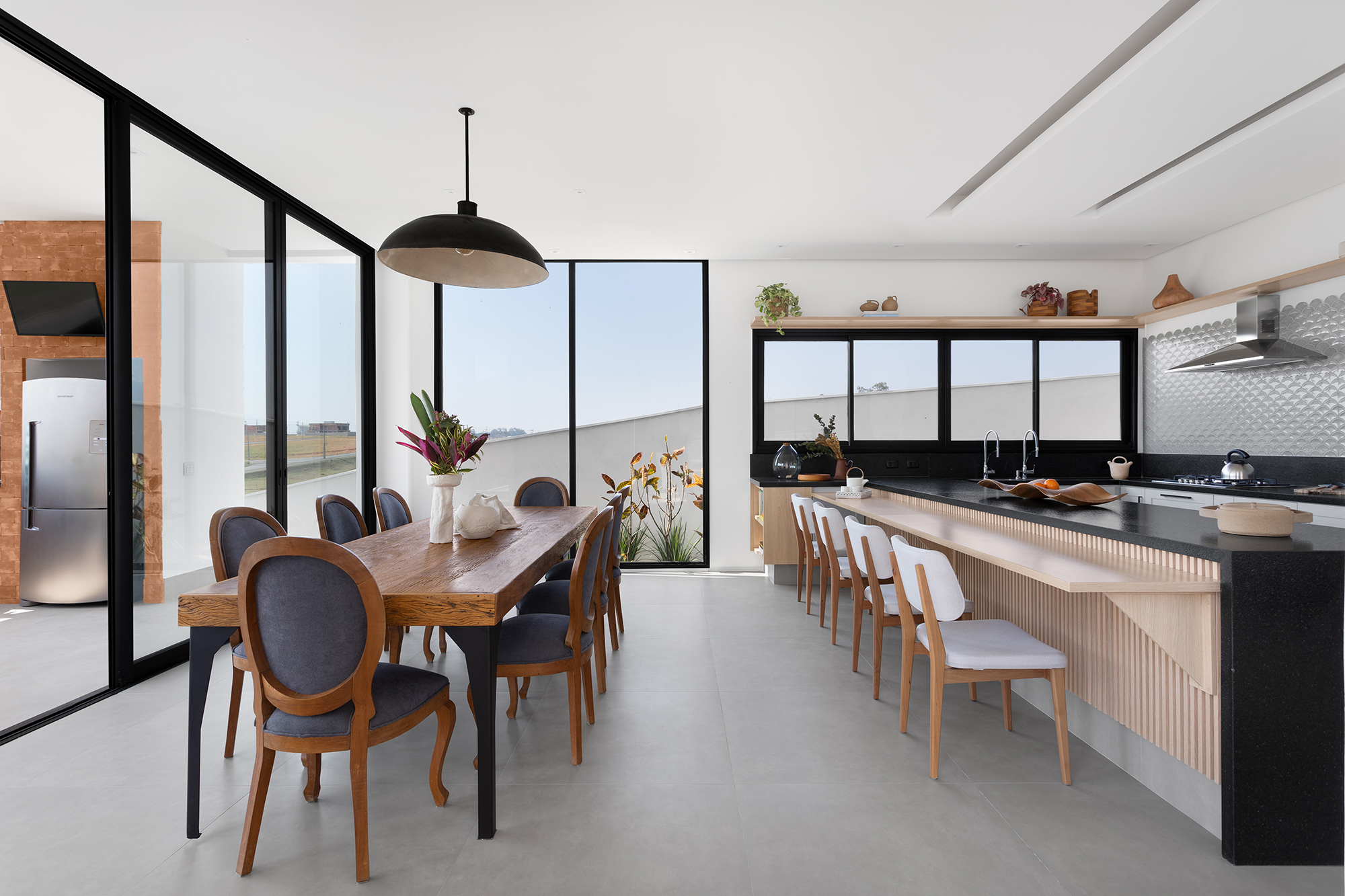 Casa de 435 m² com vista para a Serra possui piscina em formato diagonal. Projeto de Vivi Cirello. Na foto, cozinha com bancada ripada e frontão metálico.