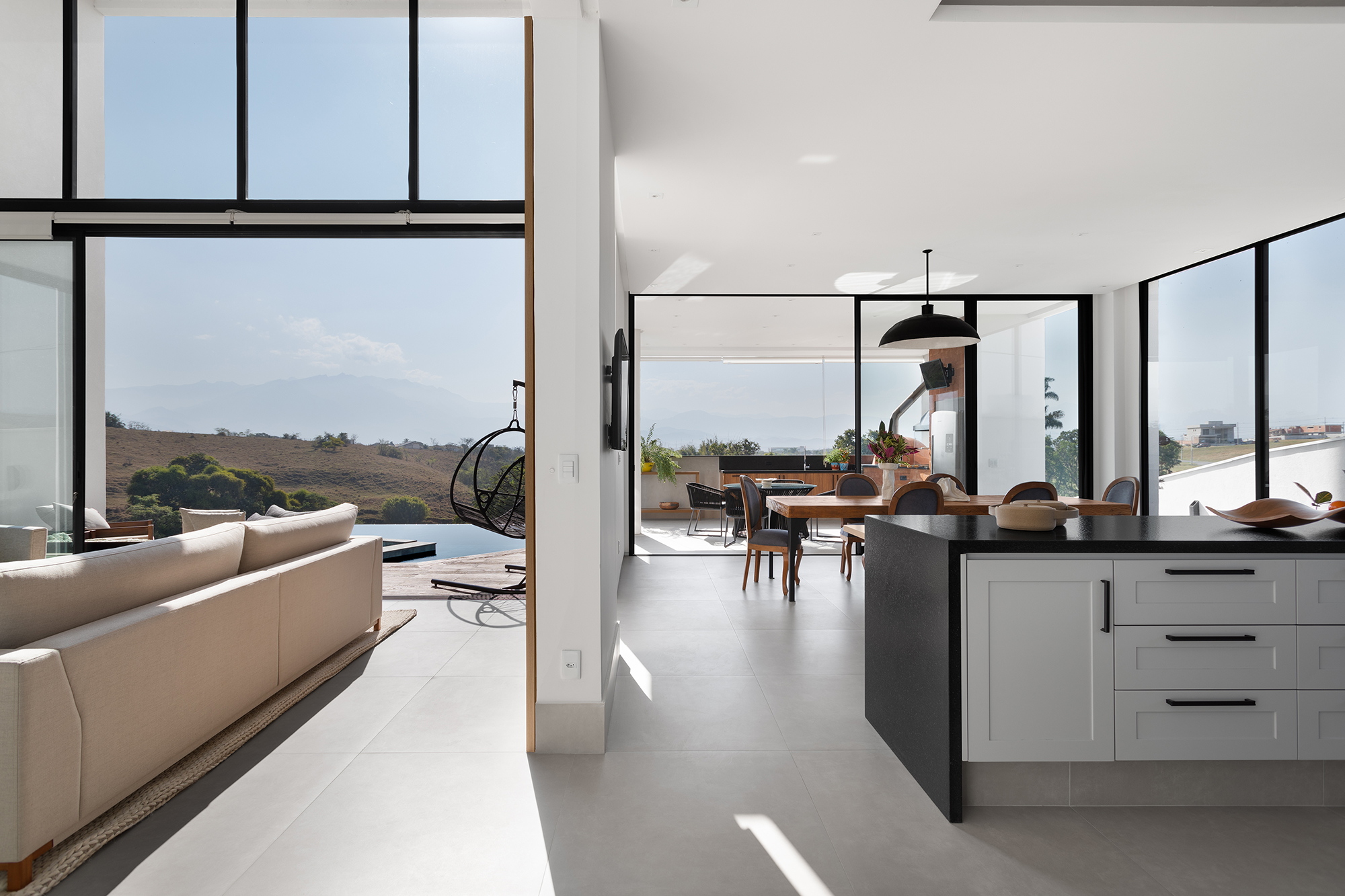 Casa de 435 m² com vista para a Serra possui piscina em formato diagonal. Projeto de Vivi Cirello. Na foto, cozinha integrada com jantar e sala.