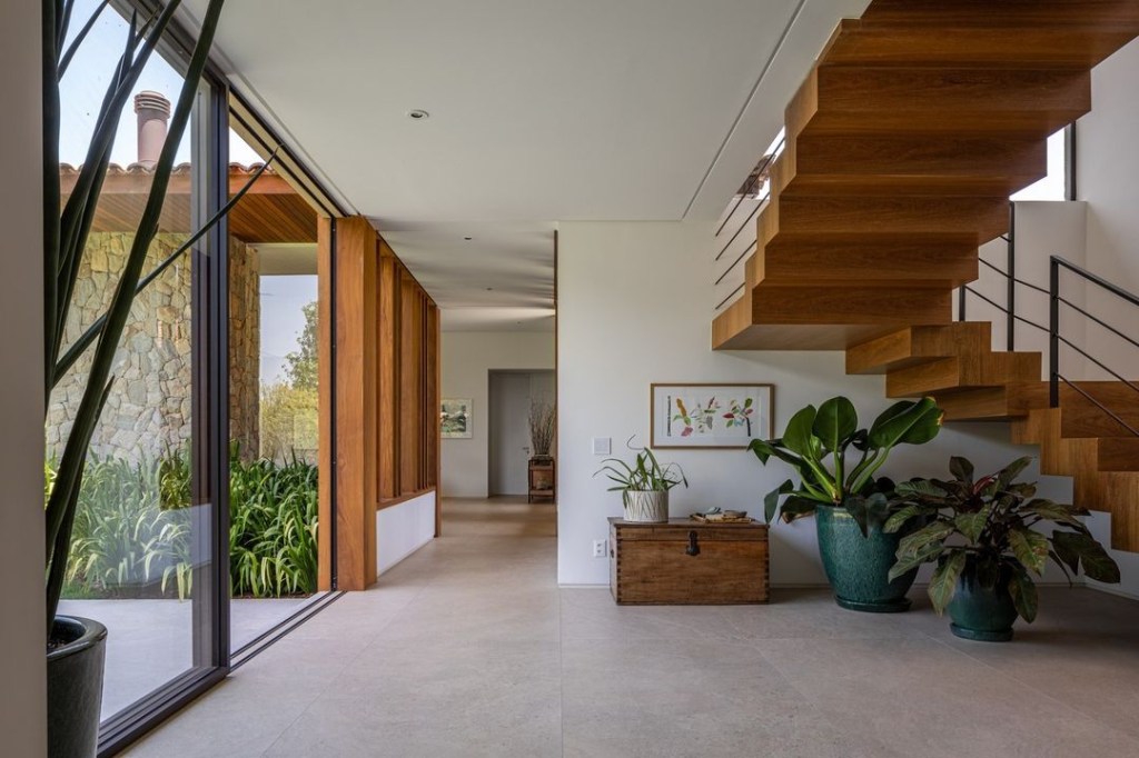 Casa de campo de 600 m² é projetada a partir da natureza do entorno. Projeto Gilda Meirelles Arquitetura. Na foto, sala com escada, vista para o jardim e vasos,