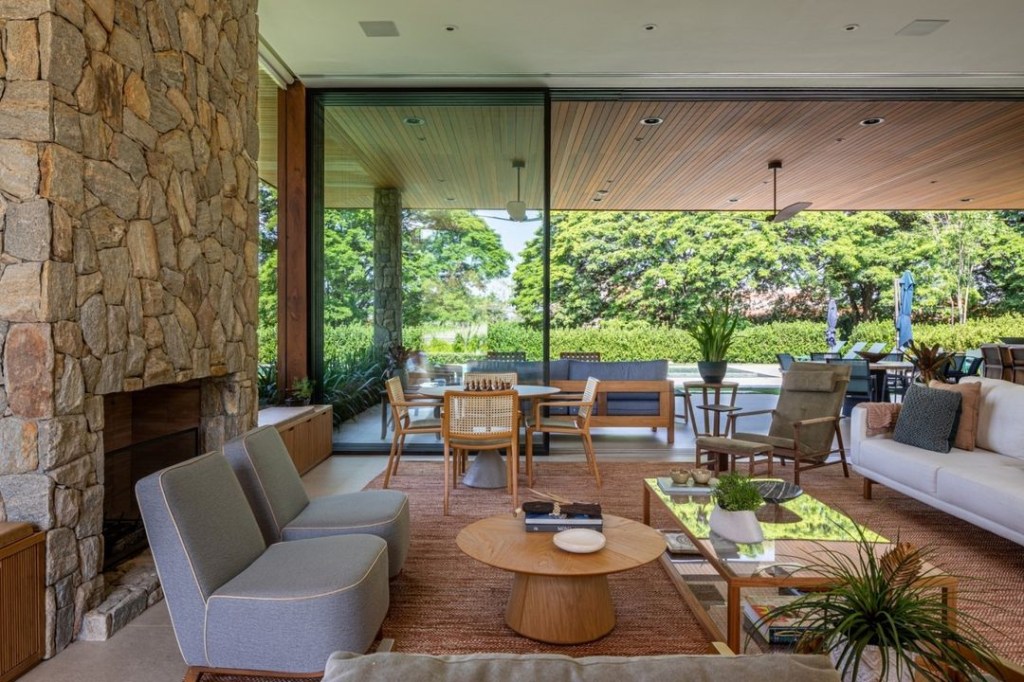 Casa de campo de 600 m² é projetada a partir da natureza do entorno. Projeto Gilda Meirelles Arquitetura. Na foto, varanda e sala integradas, lareira e estar.