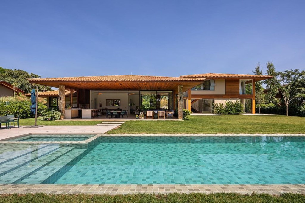 Casa de campo de 600 m² é projetada a partir da natureza do entorno. Projeto Gilda Meirelles Arquitetura. Na foto, jardim e piscina integrados, varanda.