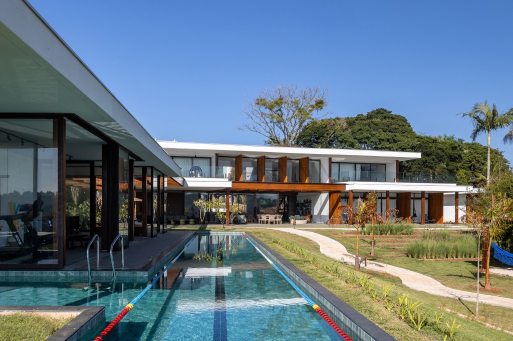 Casa é composta por três volumes ligados por pergolado de madeira. Projeto de Arkitito. Na foto, área externa de casa, raia, piscina.
