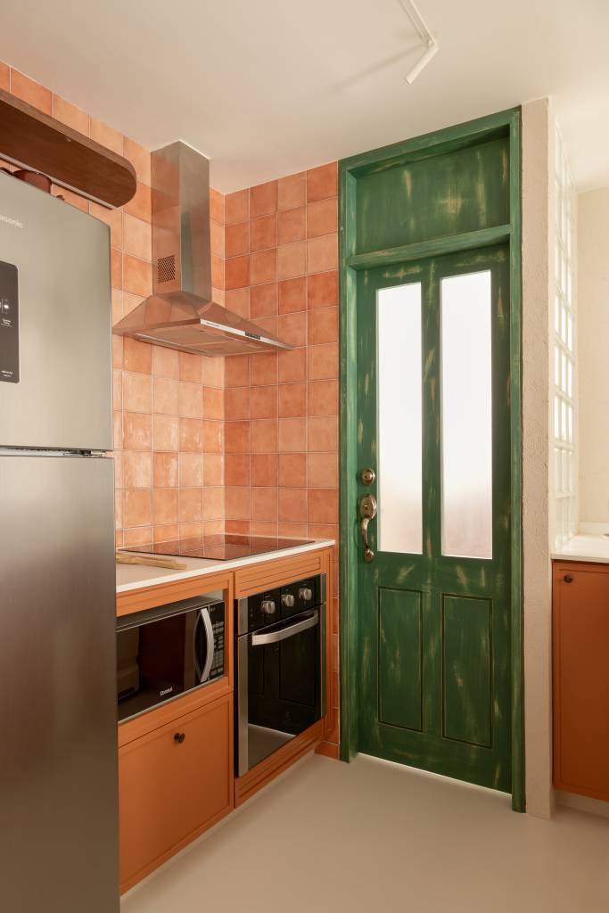 Com 33 m², studio com toque vintage usa tijolos de vidro como divisória. Projeto de Mariana Monnerat. Na foto, cozinha com azulejos terracota, porta verde.