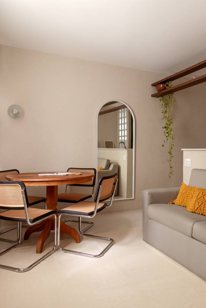 Com 33 m², studio com toque vintage usa tijolos de vidro como divisória. Projeto de Mariana Monnerat. Na foto, sala de jantar pequena com mesa redonda, espelho, sofá cinza.