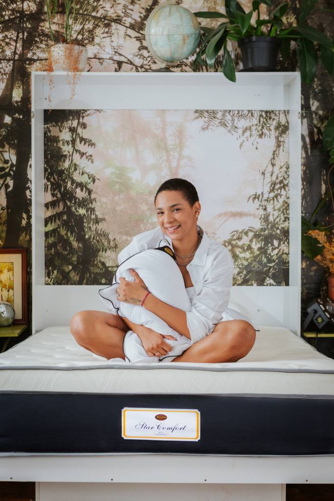 Como a escolha da cama influencia na decoração do quarto. Na foto, pessoa sentada em cama abraçando travesseiro.