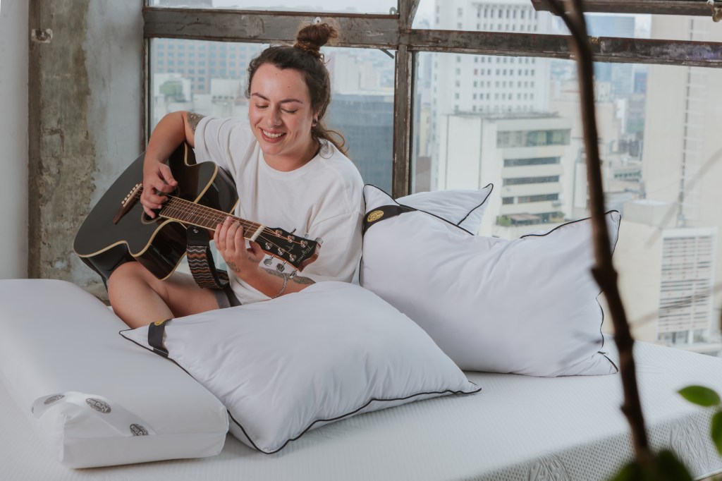 Como a escolha da cama influencia na decoração do quarto. Na foto, pessoa tocando violão na cama.