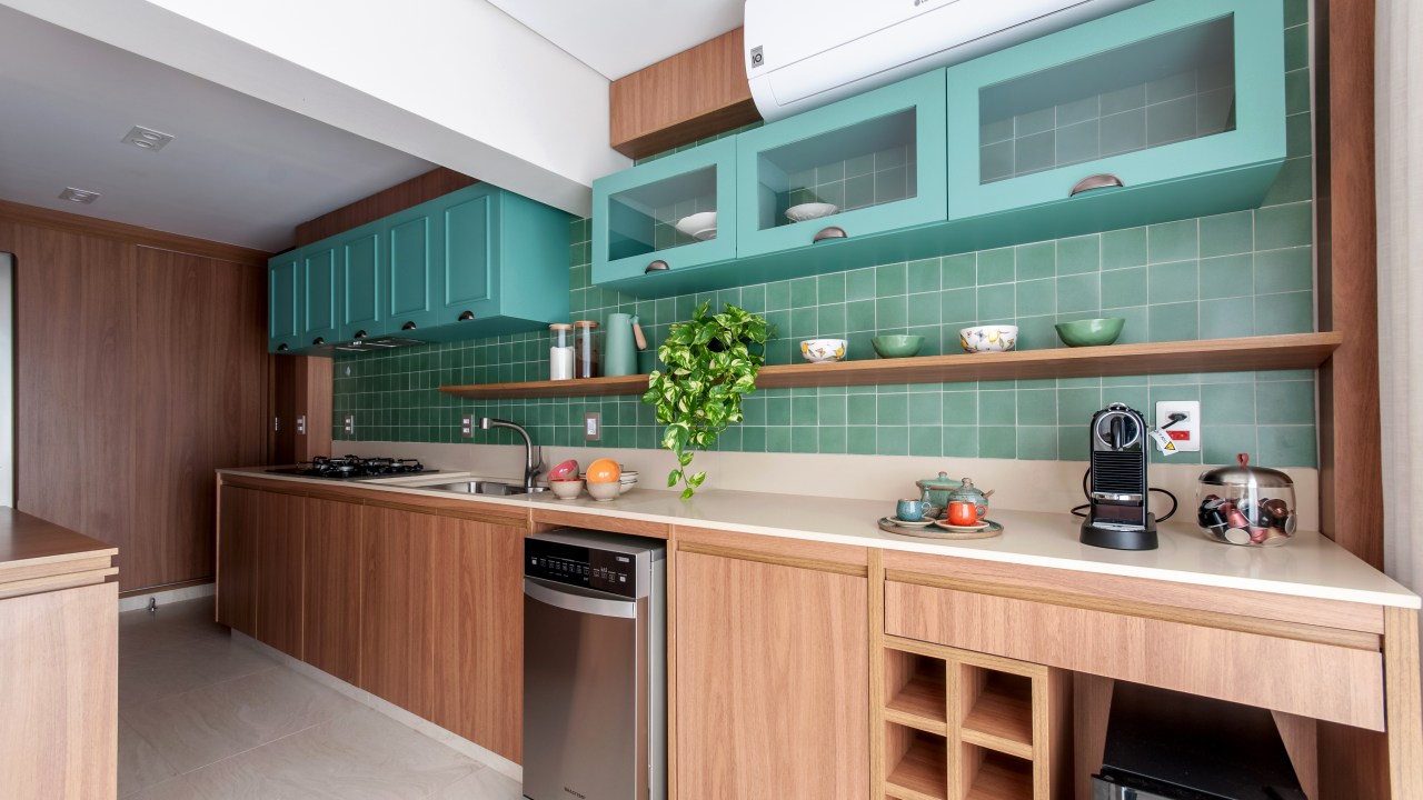 Cozinha com armários e revestimentos verde azulados é o charme deste apê. Projeto de Paiva e Passarini. Na foto, cozinha linear com azulejos azul esverdeados.