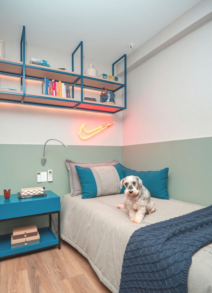 Cristaleira piso-teto rouba a cena na sala de jantar desta cobertura. Projeto de Paula Muller. Na foto, quarto infantil, neon com símbolo da nike, mesa lateral azul, cachorro na cama.