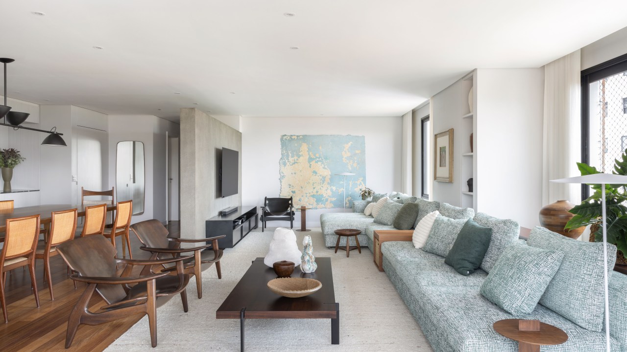 Design e cozinha com piso de ladrilho verde são destaque em apê. Projeto de TODOS Arquitetura. Na foto, sala de estar, sofá grande modular, tapete bege, tapeçaria na parede.