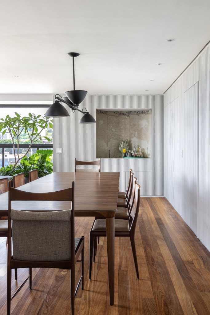 Design e cozinha com piso de ladrilho verde são destaque em apê. Projeto de TODOS Arquitetura. Na foto, sala de jantar, mesa de madeira, luminária preta, painel ripado branco.