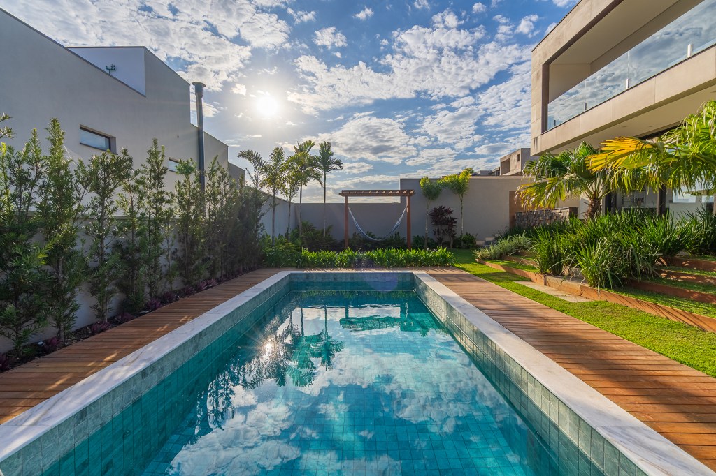 Grandes vãos de vidro integram esta casa de 600 m² à natureza do entorno. Projeto Beth Araújo. Na foto, jardim com pergolado e piscina.
