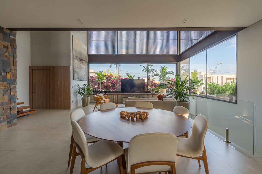 Grandes vãos de vidro integram esta casa de 600 m² à natureza do entorno. Projeto Beth Araújo. Na foto, sala de jantar e estar com pé-direito duplo e vista para o jardim.