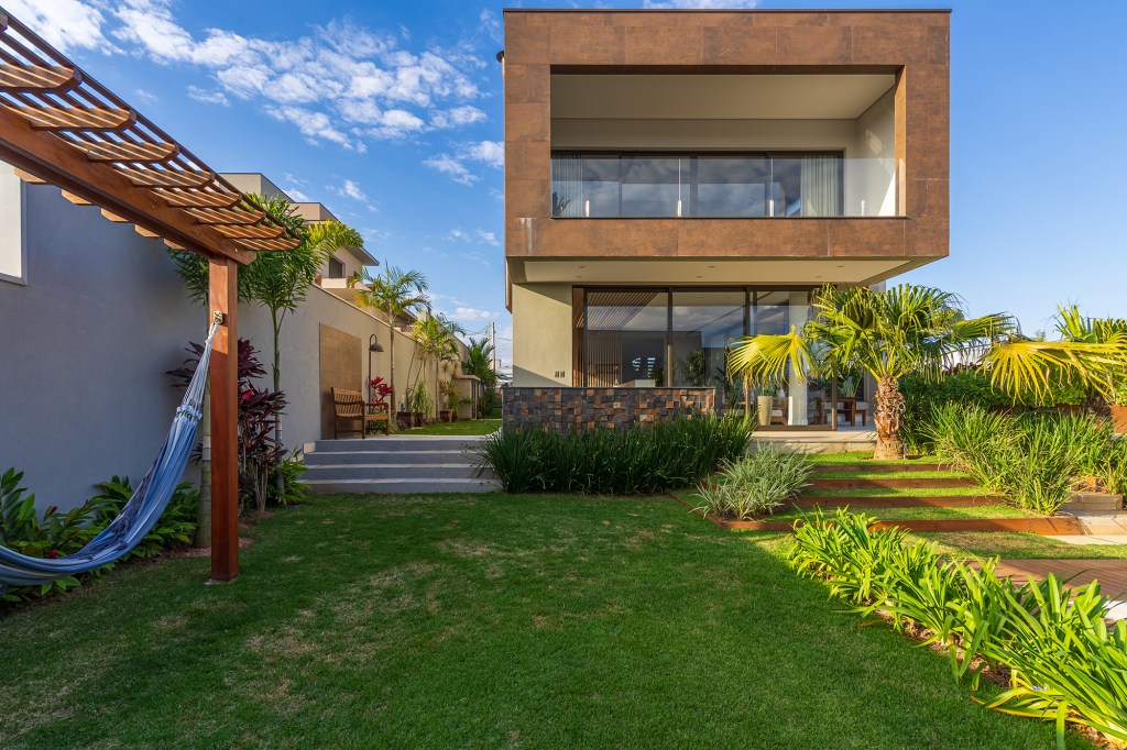 Grandes vãos de vidro integram esta casa de 600 m² à natureza do entorno. Projeto Beth Araújo. Na foto, fachada com jardim e pergolado.