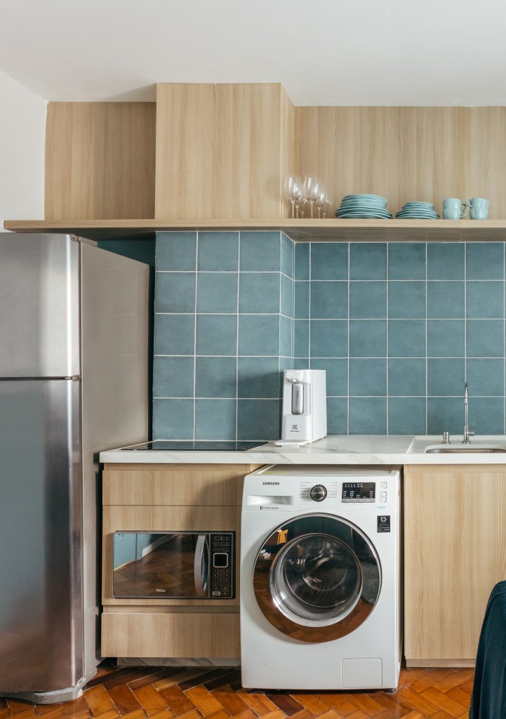 Microapê com 25 m² ganha tons azuis com reforma de apenas 3 meses. Projeto de Rodolfo Consoli. Na foto, loft com parede de revestimento cerâmico azul abrigando lavanderia, cozinha e tv. Máquina de lavar.