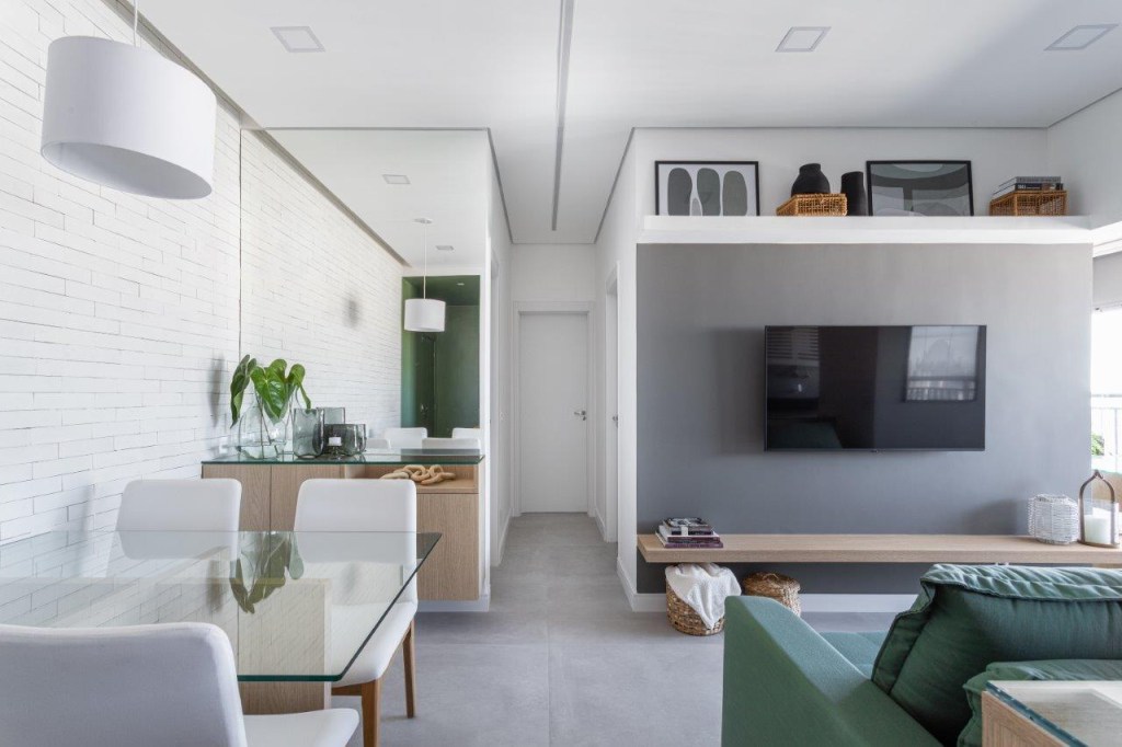 Sofá retrátil verde é destaque na sala de estar deste apartamento de 67 m². Projeto de Ju Miranda. Na foto, sala de estar e jantar integradas, espelho, parede cinza, corredor para área íntima.