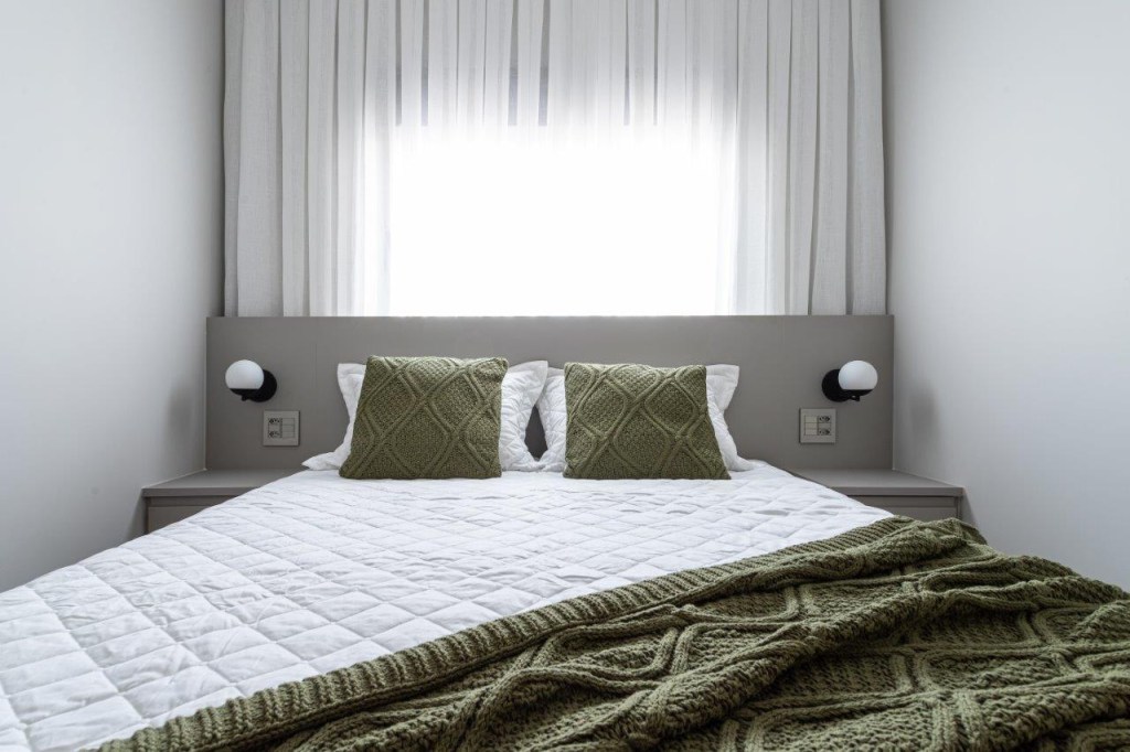 Sofá retrátil verde é destaque na sala de estar deste apartamento de 67 m². Projeto de Ju Miranda. Na foto, quarto com cama de casal, cortina e cabeceira cinza.