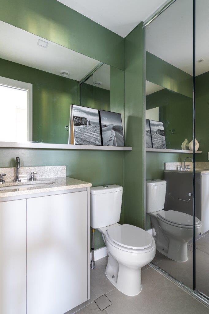 Sofá retrátil verde é destaque na sala de estar deste apartamento de 67 m². Projeto de Ju Miranda. Na foto, banheiro com parede verde e marcenaria branca.
