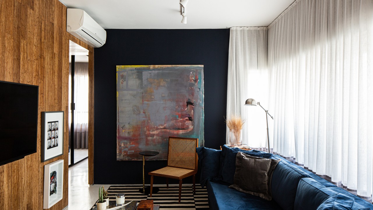 Tons de azul e ocre criam conforto e charme neste apê de 50 m². Projeto Estúdio Pluri. Na foto, sala com sofá azul e quadro.