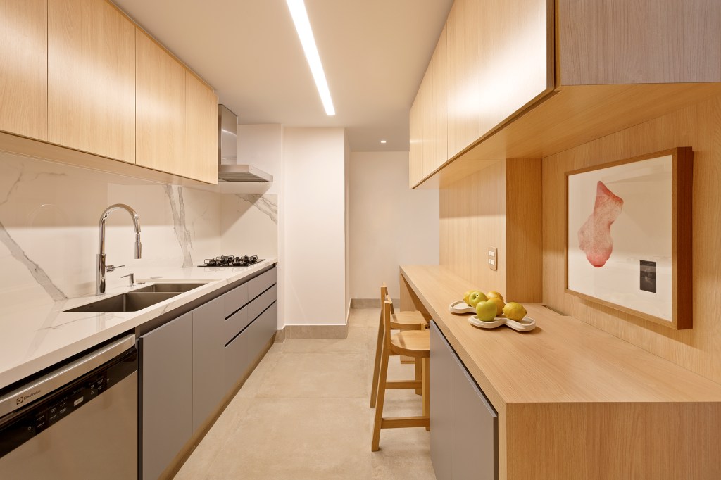 Apartamento de 151 m² ganha bar de mármore logo na entrada. Projeto de Ana Toscano Arquitetura. Na foto, cozinha com marcenaria cinza e bancada de refeições.