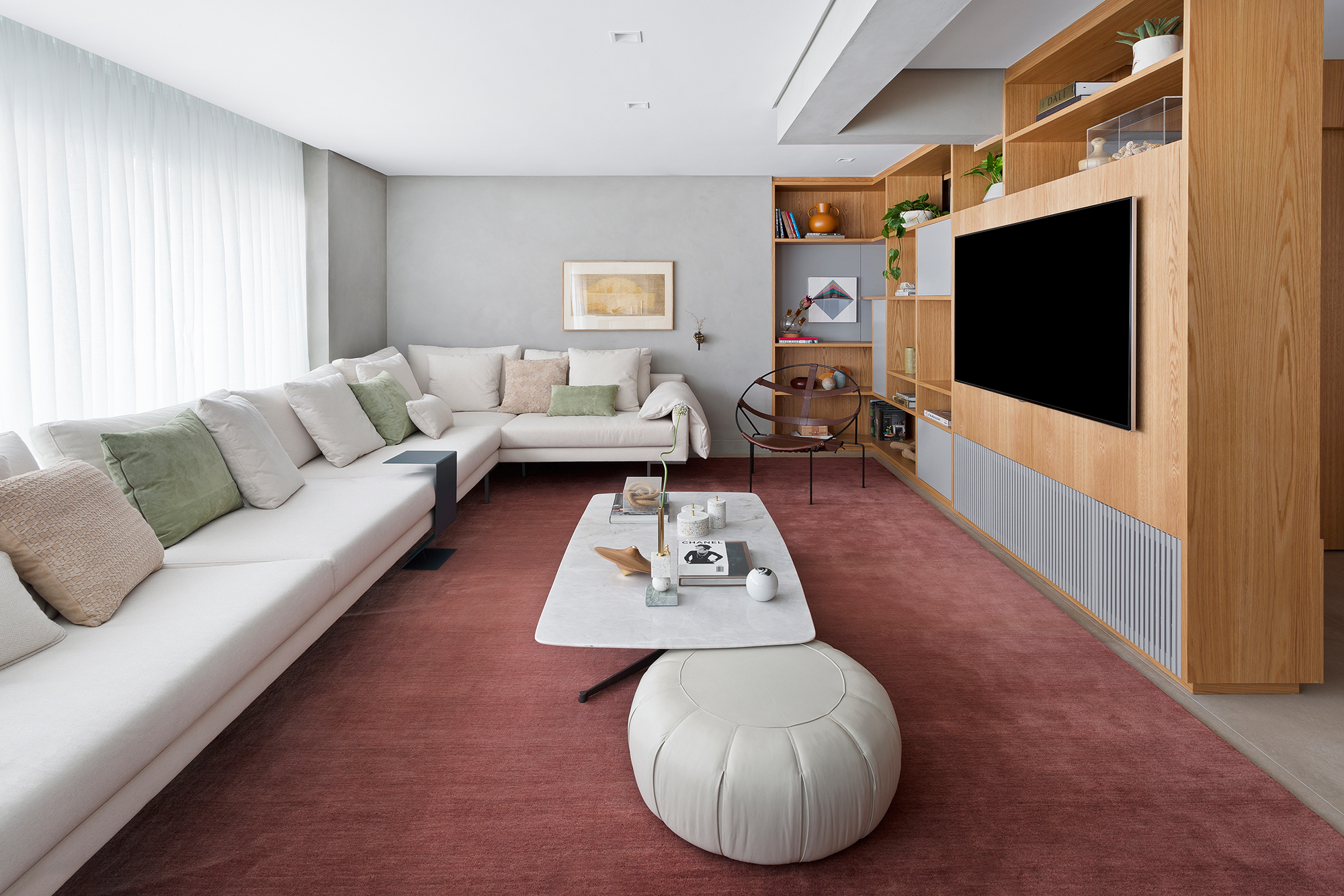 Apartamento de 151 m² ganha bar de mármore logo na entrada. Projeto de Ana Toscano Arquitetura. Na foto, sala de estar e Tv com tapete vinho, sofá e painel de madeira.