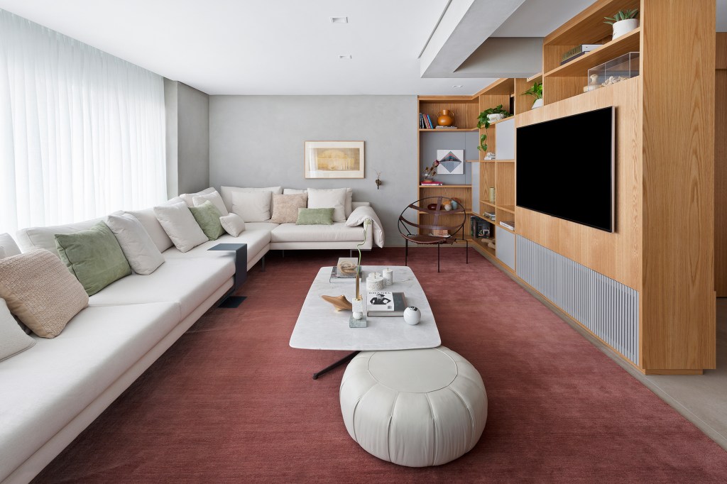 Apartamento de 151 m² ganha bar de mármore logo na entrada. Projeto de Ana Toscano Arquitetura. Na foto, sala de estar e Tv com tapete vinho, sofá e painel de madeira.
