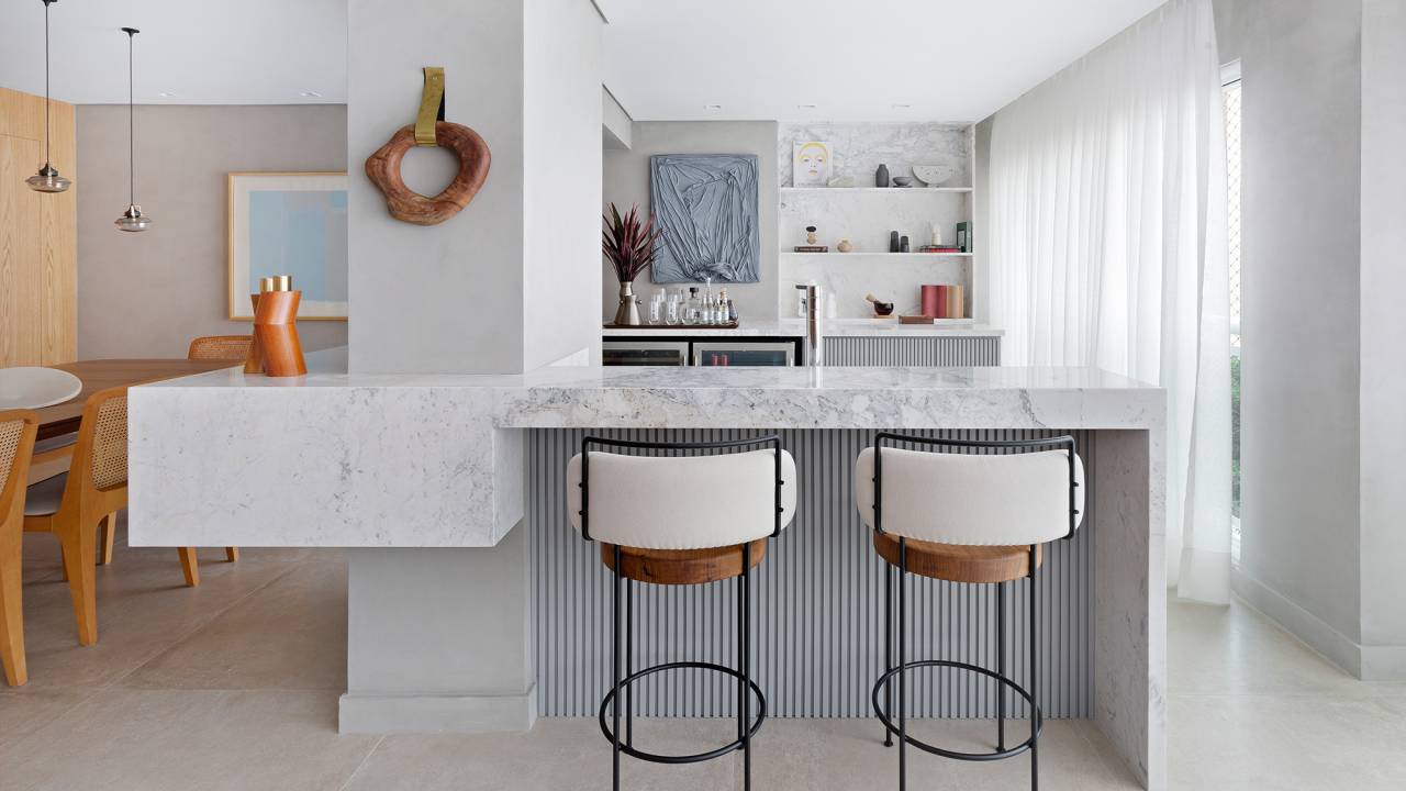 Apartamento de 151 m² ganha bar de mármore logo na entrada. Projeto de Ana Toscano Arquitetura. Na foto, bar com tampo de mármore, sala de jantar e parede de madeira,