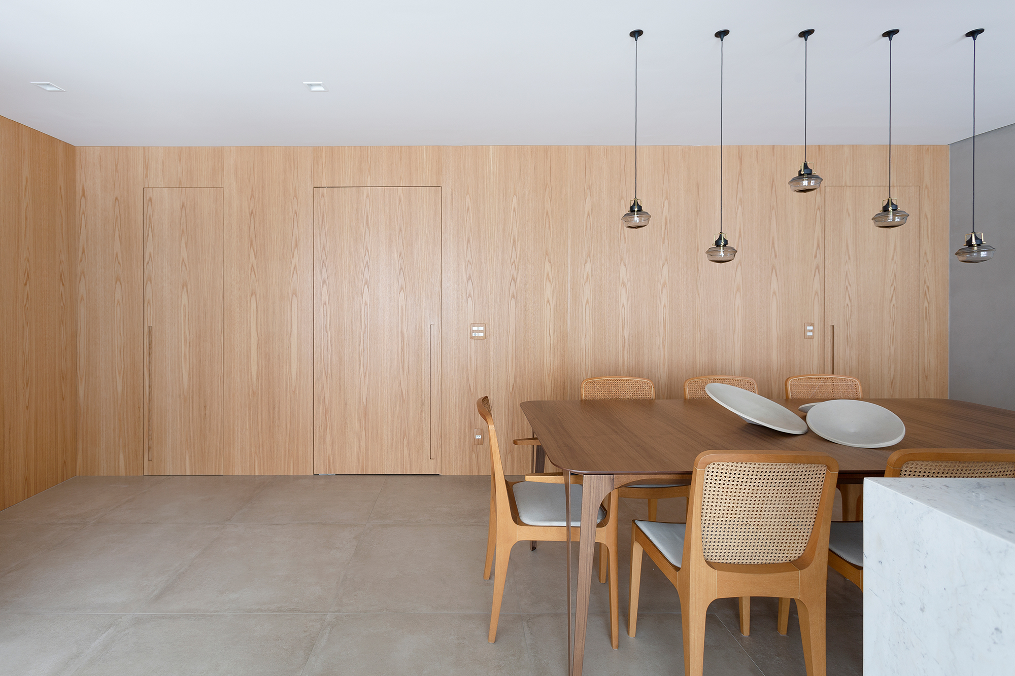 Apartamento de 151 m² ganha bar de mármore logo na entrada. Projeto de Ana Toscano Arquitetura. Na foto, sala de jantar com parede de madeira, bar e quadro.