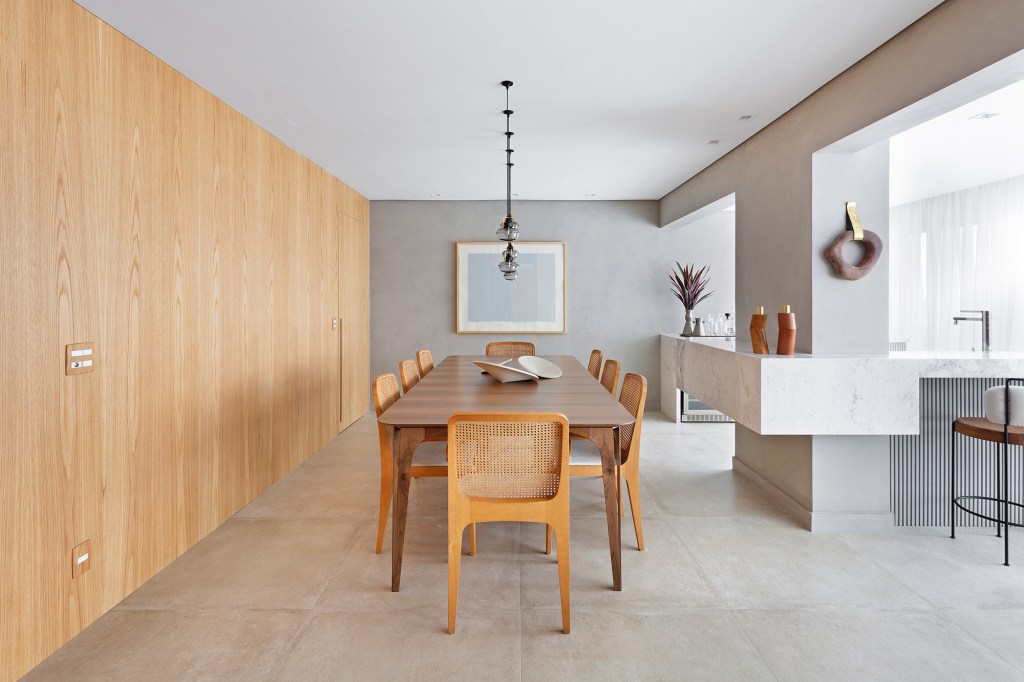Apartamento de 151 m² ganha bar de mármore logo na entrada. Projeto de Ana Toscano Arquitetura. Na foto, sala de jantar com parede de madeira, bar e quadro.