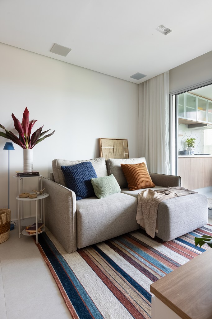 Apartamento de 83 m² ganha décor acolhedor sem derrubar nenhuma parede. Projeto do Estúdio Maré, Na foto, sala com sofá cinza chaise e tapete listrado.