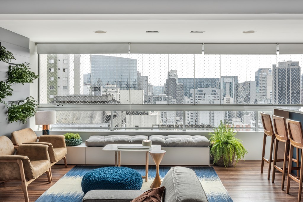 Apartamento ganha décor com tons de azul, cinza e madeira. Projeto de Beatriz Quinelato. Na foto, sala com varanda integrada e vista para a cidade.