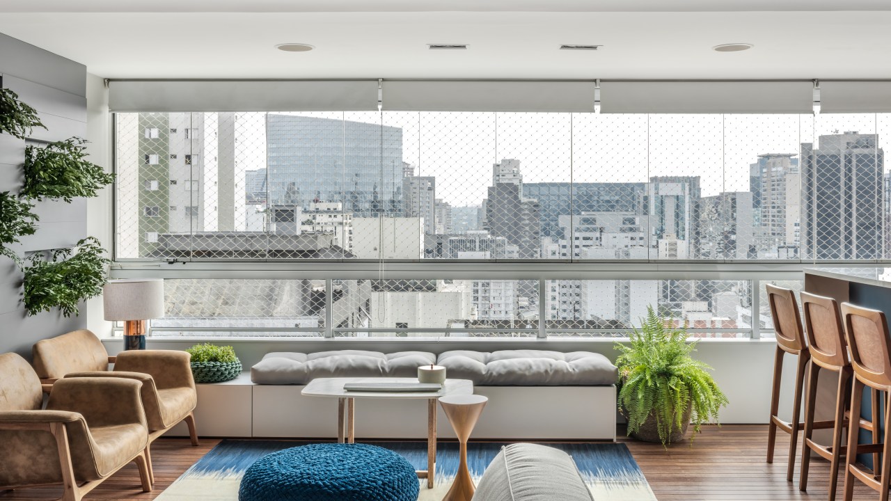 Apartamento ganha décor com tons de azul, cinza e madeira. Projeto de Beatriz Quinelato. Na foto, sala com varanda integrada e vista para a cidade.