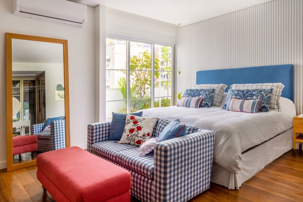Apartamento solar de 300 m² é feito para receber amigos. Projeto de Ana Veira. Na foto, quarto de casal com cabeceira azul, espelho e sofá xadrez,