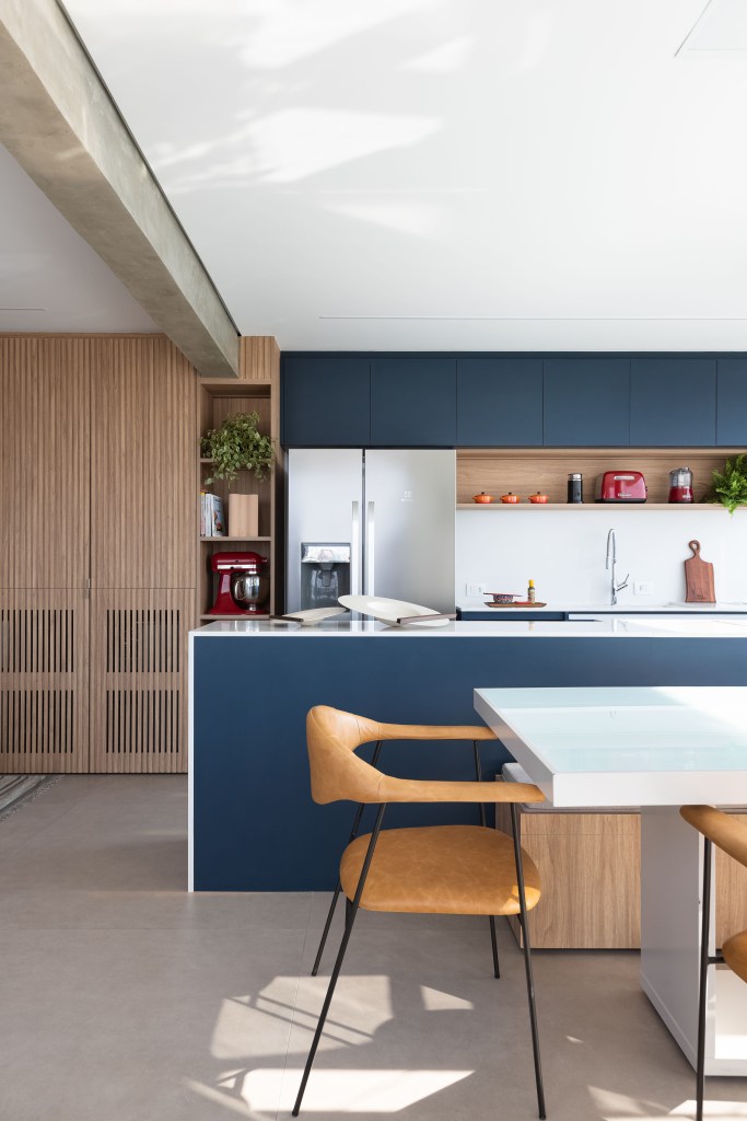 Apê de 120m² ganha cozinha integrada azul e sala de TV com porta de correr. Projeto de Carolina Gava. Na foto, cozinha integrada, armário azul, mesa de jantar branca.