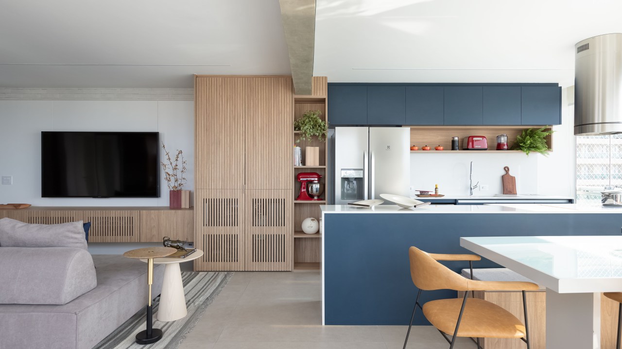 Apê de 120m² ganha cozinha integrada azul e sala de TV com porta de correr. Projeto de Carolina Gava. Na foto, cozinha americana, armários azuis.