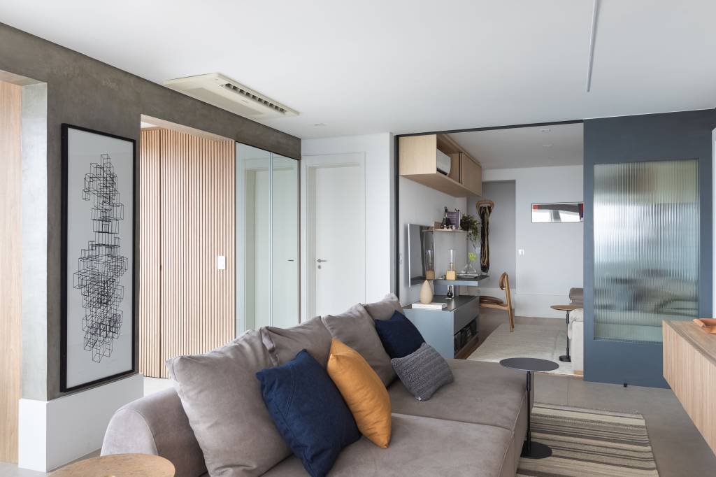 Apê de 120m² ganha cozinha integrada azul e sala de TV com porta de correr. Projeto de Carolina Gava. Na foto, home office, porta de correr, sofá ilha cinza, tapete listrado.