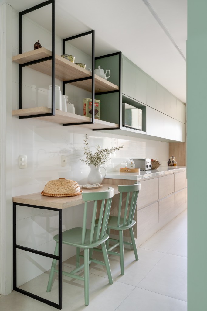 Apê de 150 m² ganha cozinha em tom verde suave e estante vazada na sala. Projeto de Ana Cano. Na foto, bancada para refeições. cadeiras verdes.
