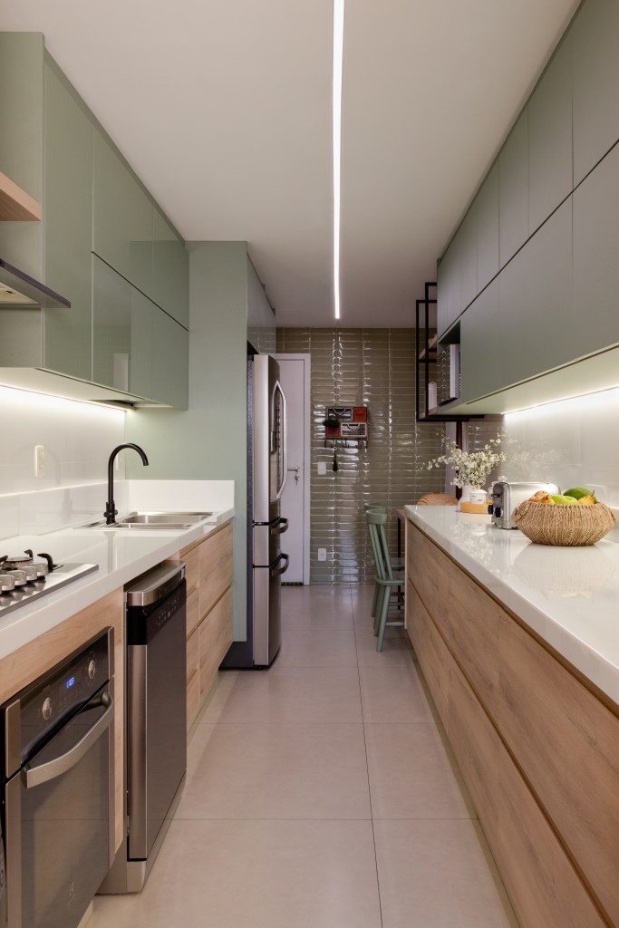 Apê de 150 m² ganha cozinha em tom verde suave e estante vazada na sala. Projeto de Ana Cano. Na foto, cozinha estreita, bancada branca.