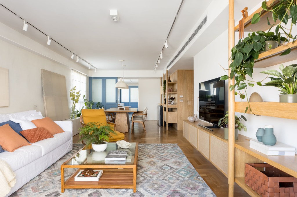 Apê de 180 m² ganha azul na marcenaria e nos revestimentos da cozinha. Projeto de Studio LAK. Na foto, sala de estar, tapete colorido, estante de madeira clara com plantas, sofá branco, mesa de centro.
