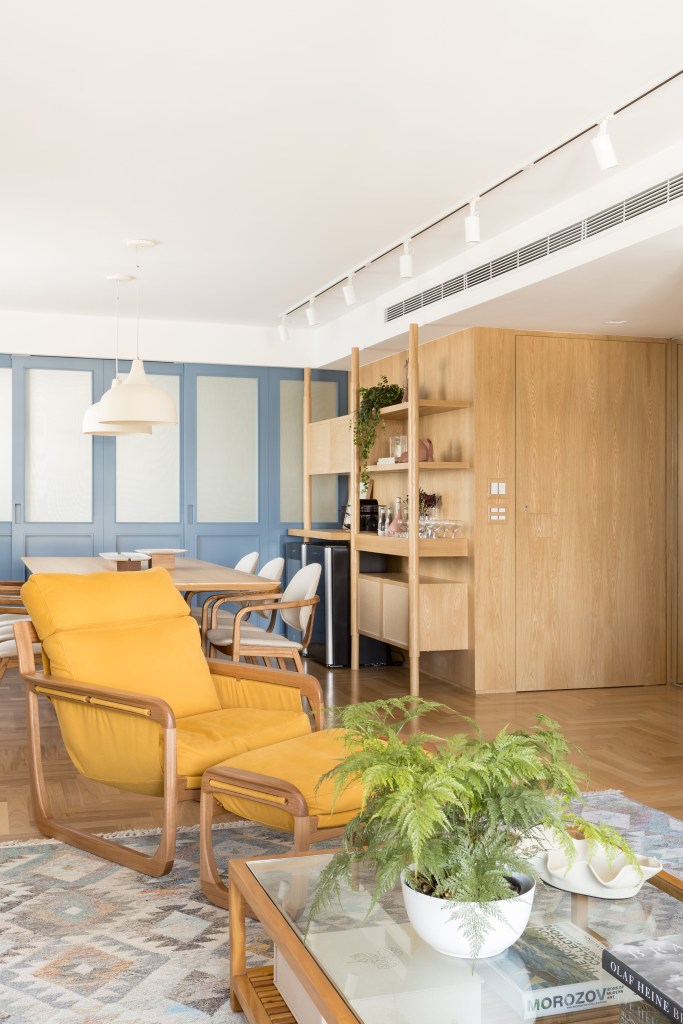 Apê de 180 m² ganha azul na marcenaria e nos revestimentos da cozinha. Projeto de Studio LAK. Na foto, sala de estar, poltrona mostarda com pufe, mesa de centro, planta, porta de correr.