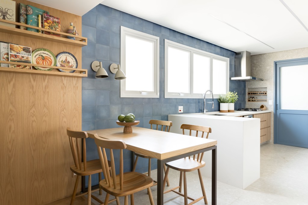 Apê de 180 m² ganha azul na marcenaria e nos revestimentos da cozinha. Projeto de Studio LAK. Na foto, painel de madeira com duas prateleiras, parede de azulejos, copa de cozinha, bancada branca.