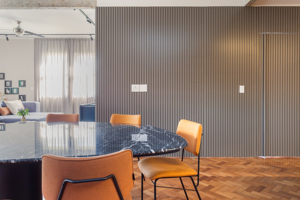 Apê de 192 m² mescla estilos industrial e brutalista com pitadas de cor. Projeto de Zimbro Arquitetura. Na foto, sala de jantar com mesa de pedra e parede ripada.