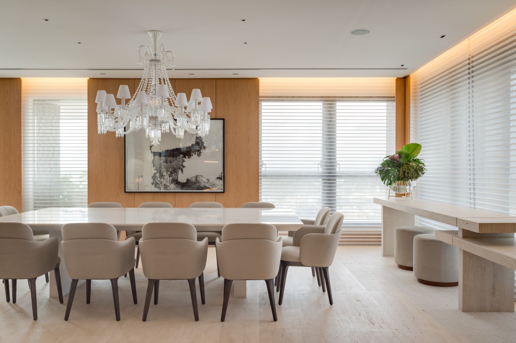 Apê de 580 m² ganha closet espelhado, área gourmet e hall marcante. Projeto de Andrea Teixeira. Na foto, sala de jantar, mesa grande branca, lustre, persiana.