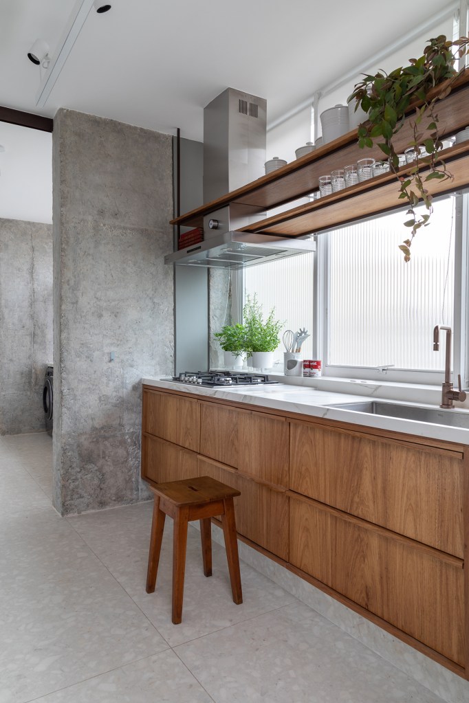 Apê dos anos 1960 é modernizado com dog shower e pilar no meio da sala. Projeto de Casa33 Arquitetura, Na foto, cozinha com prateleira suspensa e parede de concreto.